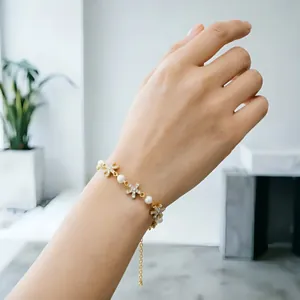 Elegante bracciale in oro con perle bianche e ciondoli floreali scintillanti sul polso