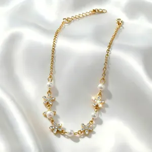 Dettaglio collana dorata con perle e ciondoli a fiore di cristallo su seta bianca.