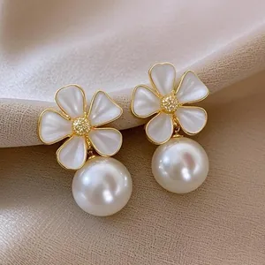 Close-up of white enamel flower stud earrings with large pearls on soft fabric background