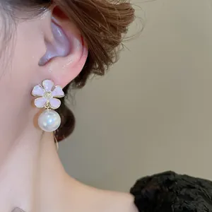 Detail view of an elegant pink enamel flower and white pearl drop earring on a model's ear