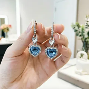 Dettaglio di orecchini a forma di cuore blu con cristalli tenuti in mano dal vivo.