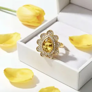 Macro di un anello di lusso in oro con gemma gialla a goccia e corona di cristalli bianchi.