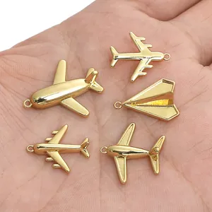 Gold airplane and paper plane charms for DIY jewelry making displayed on a hand.