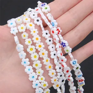 Hand holding colorful white plum blossom lampwork glass beads for DIY jewelry making