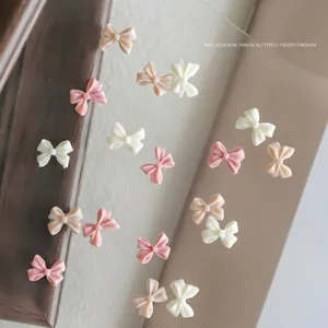 Gentle cream pink resin bow nail art charms for DIY manicures scattered on a glass surface
