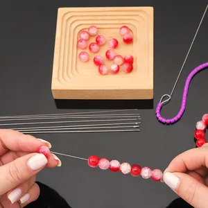 Detailed view of hands using a sharp stainless steel needle to thread red cracked beads.