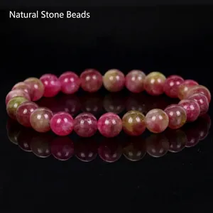 Detailed macro shot of a pink and green natural stone beaded bracelet on a reflective base