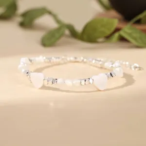 Detailed view of handmade bracelet with white heart shells and silver metallic beads.