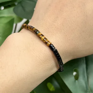 Close-up of a natural yellow tiger eye and black cylindrical bead bracelet on a wrist.