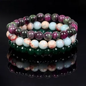 Stacked natural stone bead bracelets in mixed colors on reflective black background.