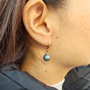 Gros plan de crochet d'oreille plaqué or 18 carats avec perle sombre irisée sur l'oreille.
