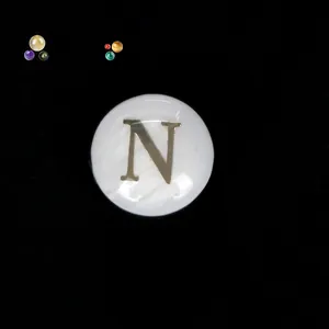 Detail einer weißen Perlmutt-Rundperle mit goldenem Buchstaben N für DIY-Schmuck.