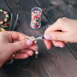 Manos usando alicates de joyería para armar una pulsera de perlas vintage con flores