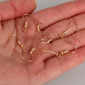 Detailed view of gold fish hook earring components on a palm for DIY jewelry making.