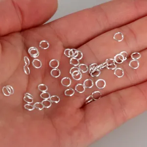 Close-up of small silver jump rings on a hand, essential for DIY jewelry making.