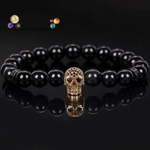 Detailed view of an 8mm black volcanic stone beaded bracelet with a gold-plated skull charm.