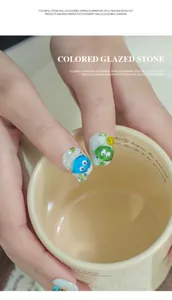 Nahaufnahme von bunter Glasstein-Nagelkunst mit niedlichen Cartoon-Monster-Dekoren.