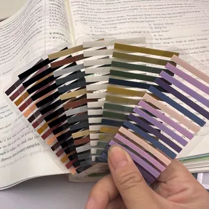 Hand holding multi-colored ultra-fine transparent PET index tabs on an open textbook page.