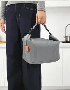 Person holding a gray insulated lunch bag with orange tag in a modern kitchen setting