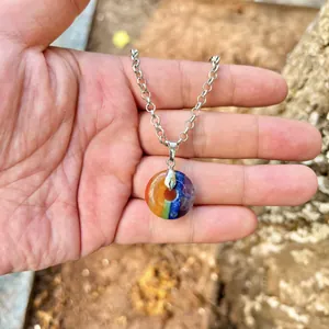Macro detail shot of a natural rainbow stone donut pendant necklace held in hand
