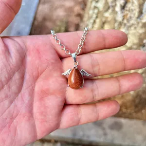 Detail view of goldstone teardrop pendant with silver angel wings held in hand