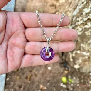 Close-up detail of a purple amethyst donut pendant on a silver chain held in hand