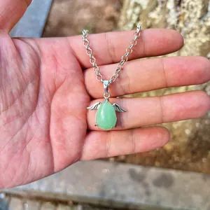 Detailed view of a green teardrop stone pendant with silver angel wings held in hand