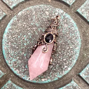 Detail of rose quartz hexagonal point pendant with ornate vintage copper wire wrap.