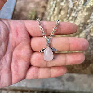 Detail of a natural rose quartz teardrop angel pendant with silver wings on a necklace