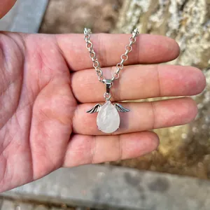 Close-up detail of a translucent white crystal angel wing pendant necklace held in hand