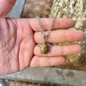 Detailed macro view of a silver angel wing natural stone pendant necklace held in palm