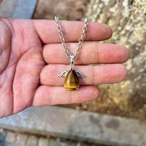 Macro view of natural tiger's eye teardrop pendant with silver angel wings in palm