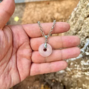 Detailed close-up of a natural rose quartz donut pendant necklace held in hand for scale