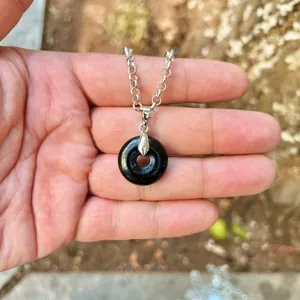 Close-up of a black natural stone donut pendant on a silver-tone chain held in hand.