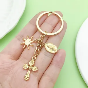 Close-up of gold-plated religious keychain with cross and sun charms held in hand