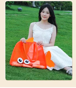 Detailed view of an orange fish-shaped mesh beach bag held by a model on a green lawn.