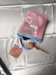 Macro view of a stylish pink mesh cosmetic bag with handheld purple strap details