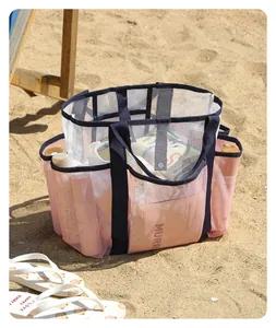 Large pink and white mesh beach bag with multiple pockets on sand.