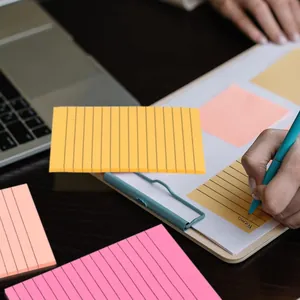 Macro view of hand writing on a lined yellow sticky note attached to a clipboard.