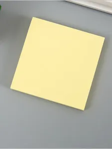 Nahaufnahme eines blassgelben quadratischen Haftnotizblocks auf grauem Hintergrund.