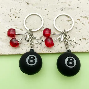 Detail view of resin cherry and 8-ball billiard charm keychains on stone background