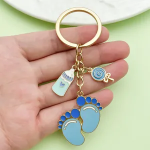 Macro detail of cute blue baby bottle and footprint enamel charms on gold keychain