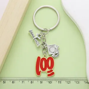 Detalle de un llavero plateado con birrete de graduación y colgante rojo de puntaje 100.