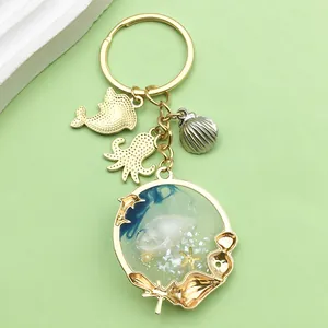 Detalle del llavero océano con colgante de concha azul y dijes de delfín y pulpo dorados