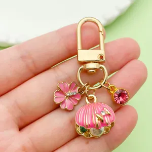 Detailed view of pink enamel shell and flower charms on a gold-plated keychain accessory