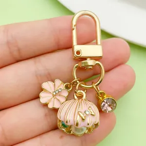 Close-up view of a golden keychain featuring pink shell, pearl and flower charms.