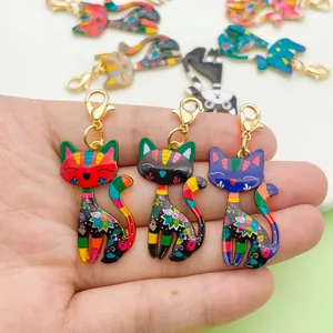 Colorful alloy cat pendants held in hand, featuring vibrant floral and striped patterns.
