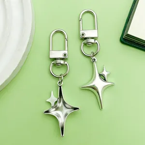 Close-up view of silver-toned alloy hollow star keychain charms on a soft green background