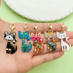 Detail of five colorful enamel cartoon cat charms held in hand for bag or key decoration.
