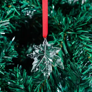 Detail of transparent maple leaf Christmas ornament hanging on green tree branch